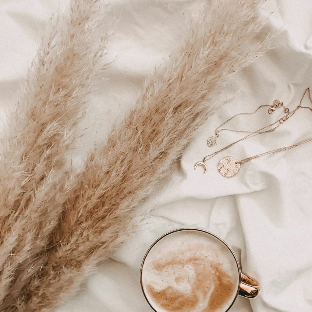 Cup of coffee with grasses lying on a bed.